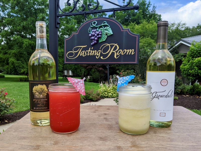 Wine bottles and wine slushies on a table with a sign for Grovedale's tasting room in the background