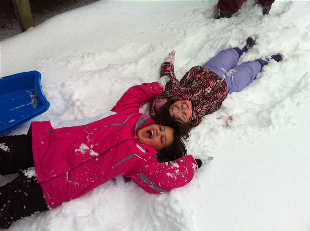 Third Place Winner - Enjoying the Snow - Photographer: Linda Mahoney. Two young children laying in the snow smiling.