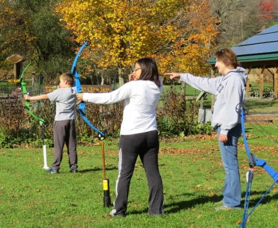 An archery instructor stands behind a woman and a boy with bows.