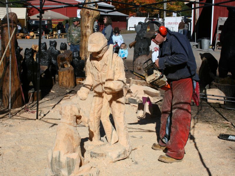 A man uses a chainsaw to carve a hunter and a dog