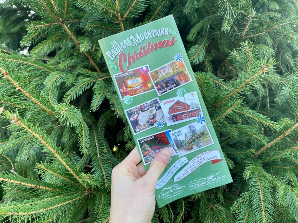 A green Endless Mountains Christmas brochure against a background of pine boughs