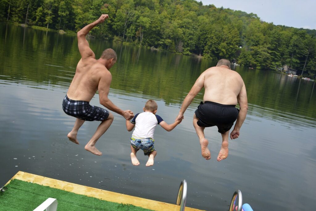 Two men and a boy jump off a dock into a lake