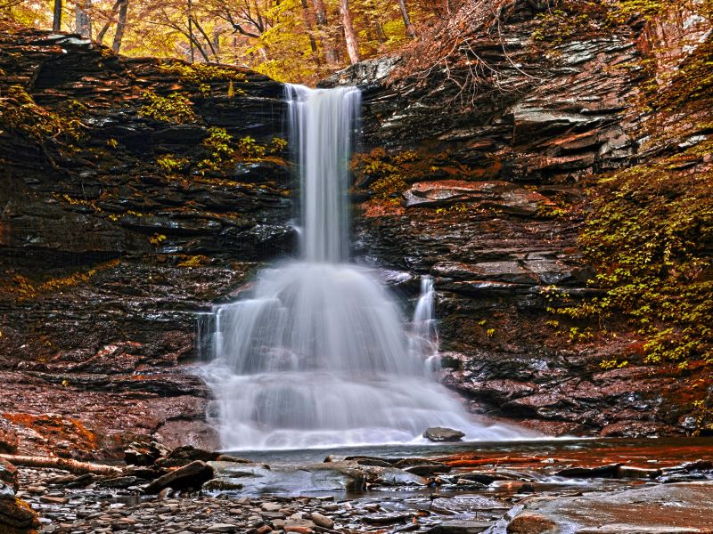 A waterfall surrounded by rocks and yellow fall foliage