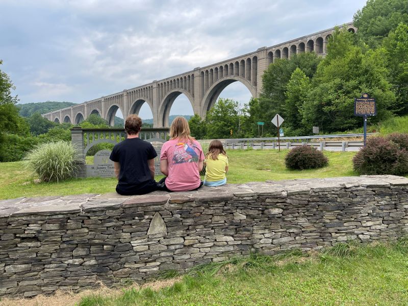 Three kids sit on a stone wall looking at the Tunkhannock Creek Viaduct