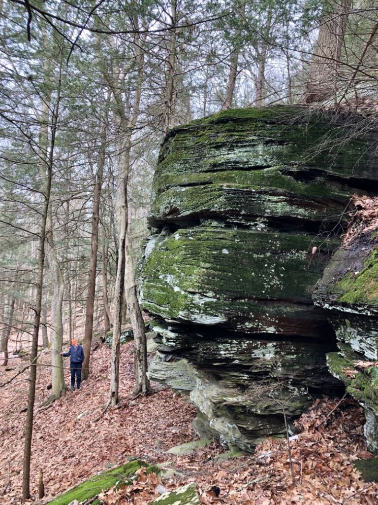 A hiker stands next to large rock formations at the Peck Preserve